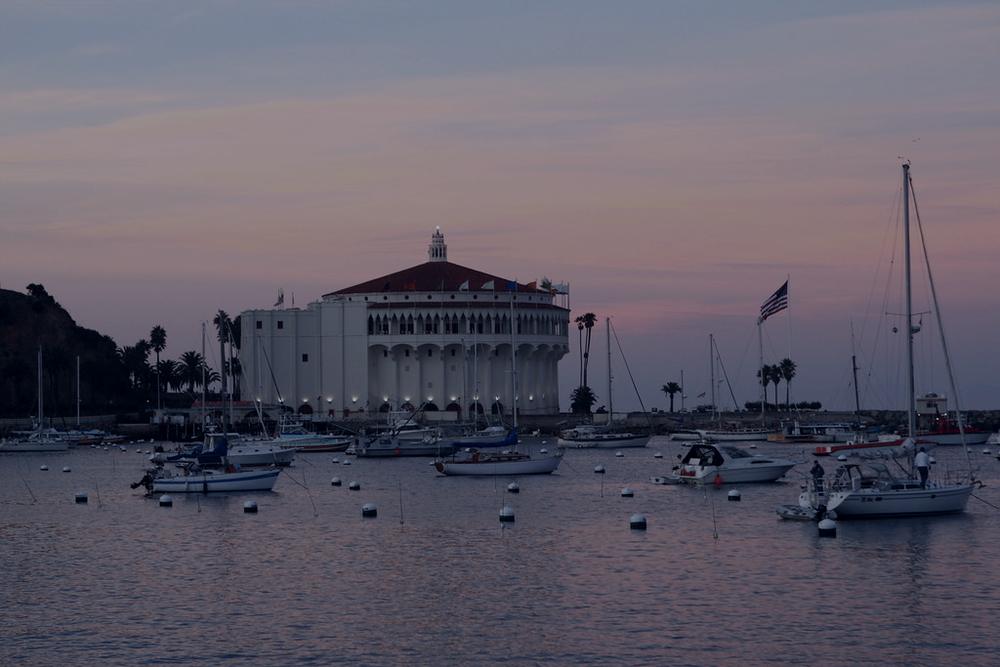 The Avalon Casino at dusk, lit up across the harbor with moored boats in front